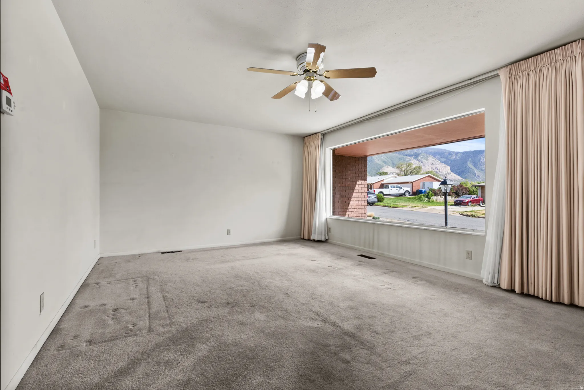 Expansive window with mountain backdrop, ceiling fan, and wall-to-wall carpeting