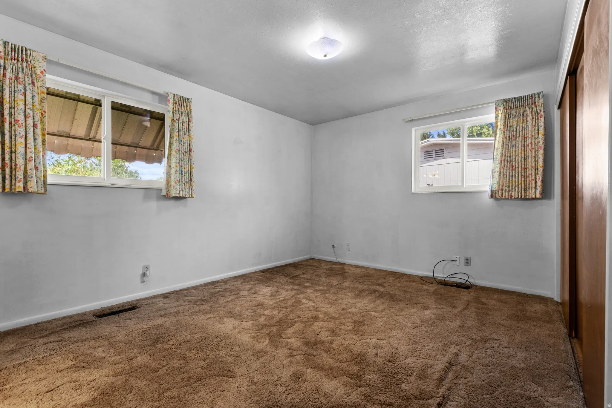 Spacious bedroom with abundant natural light from dual windows, warm wood-finish flooring, and fresh white walls throughout