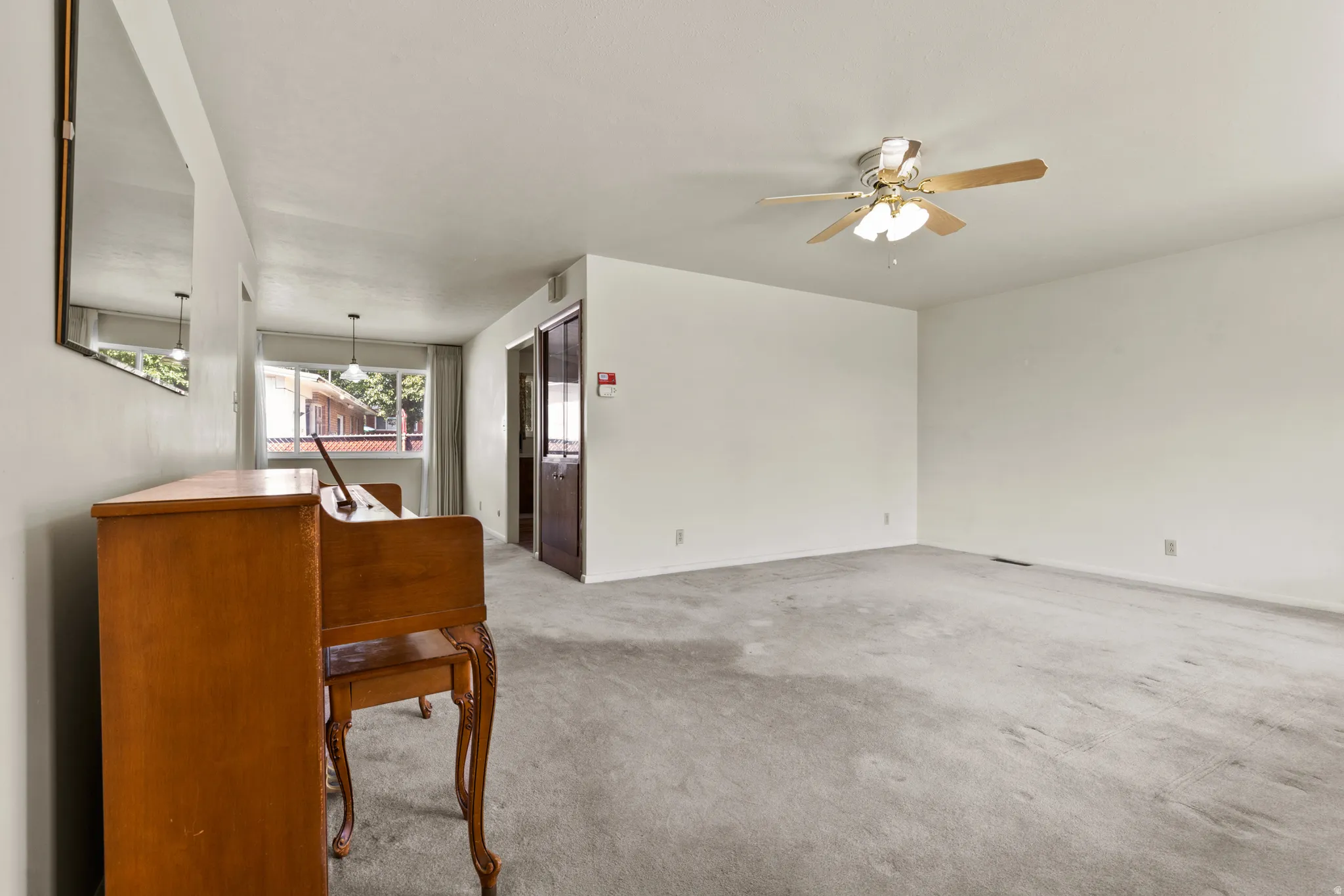 Carpeted living area with a ceiling fan light fixture and a large window
