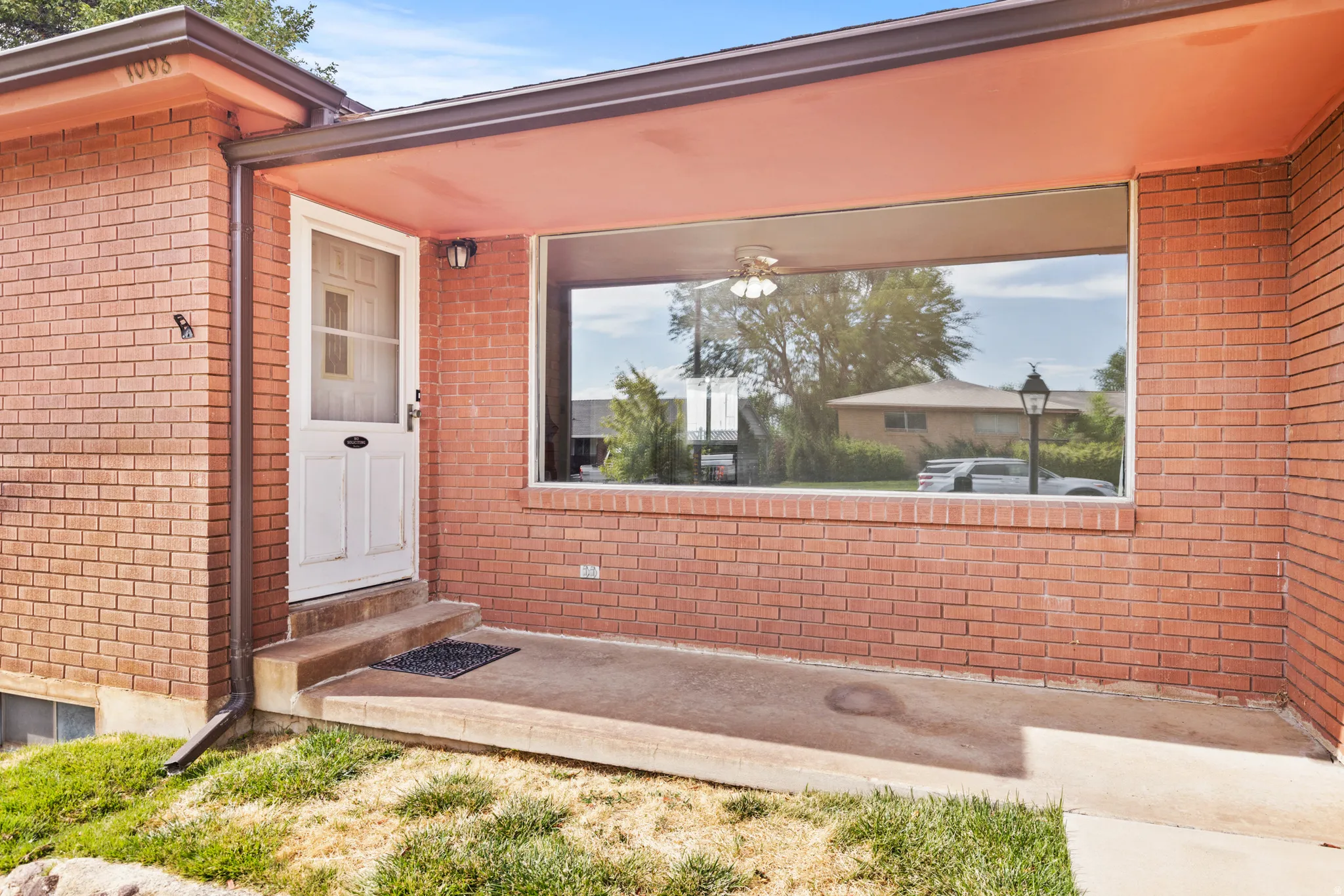 Brick exterior with a large picture window, covered entryway, concrete porch, and white paneled door