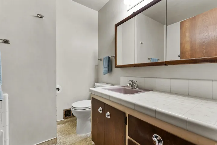 Spa-inspired bathroom featuring dual vanity with wood-finish cabinetry, white tile countertop, and polished chrome fixtures