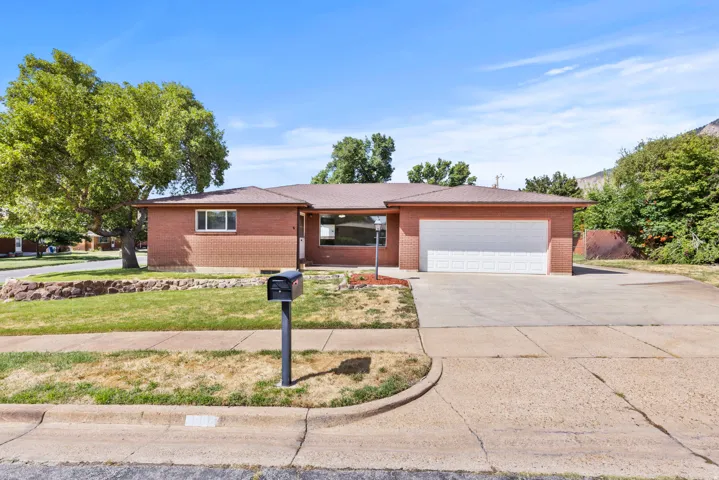 Brick exterior with an attached garage, paved driveway, and established trees