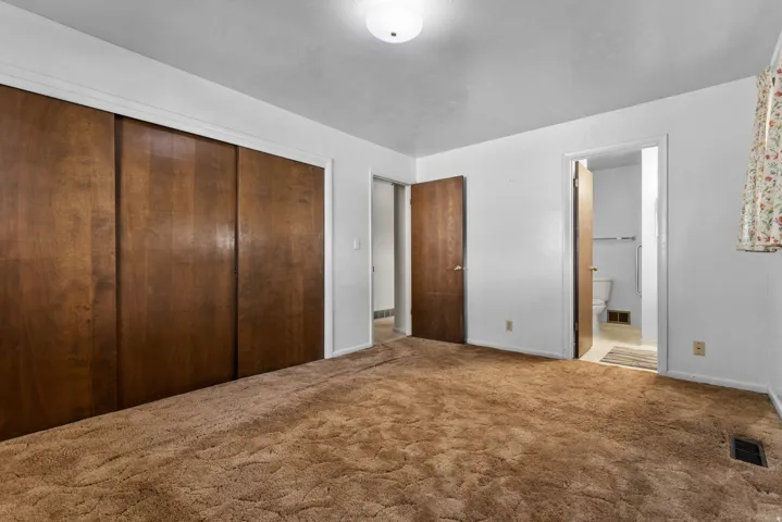 Spacious primary bedroom suite with triple wood-finish closet doors, neutral carpeting, and multiple entry points including direct access to an ensuite bathroom