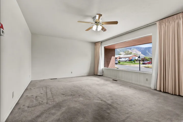 Expansive window with mountain backdrop, ceiling fan, and wall-to-wall carpeting