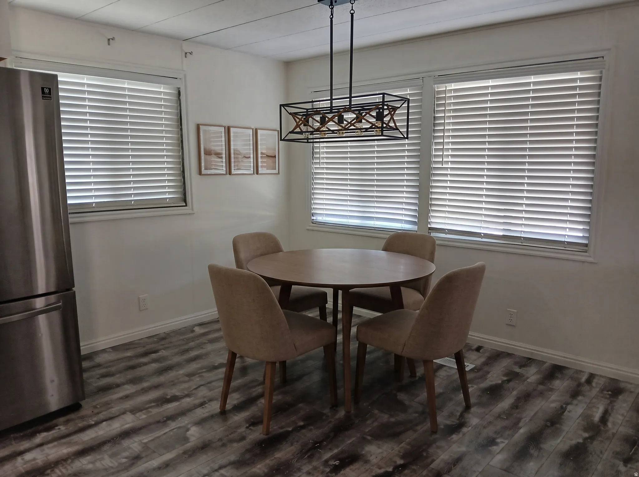 Spacious dining area featuring wood-finish flooring, multiple windows with blinds, and a contemporary linear chandelier
