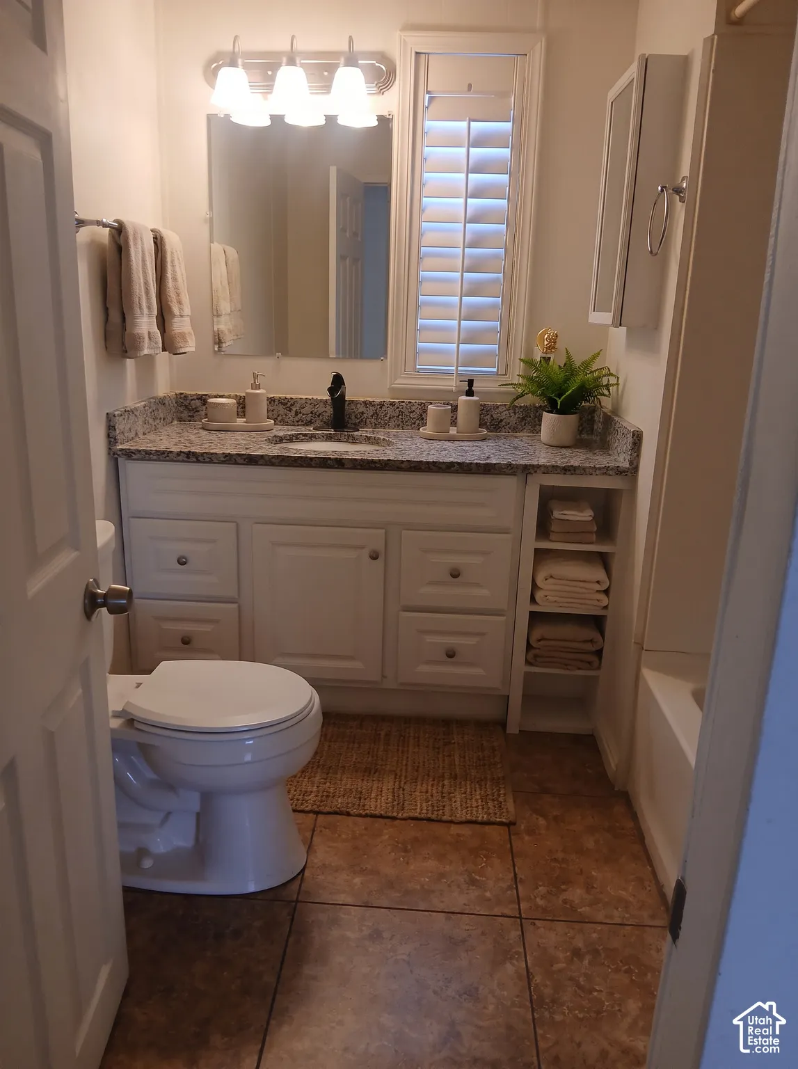 Dual-sink vanity with a light granite countertop, white cabinetry, and matte black faucets