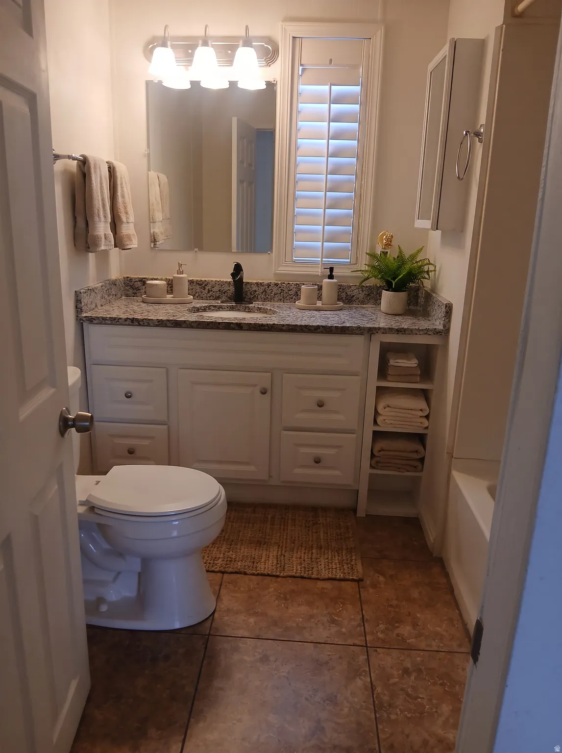 White vanity with dual sinks, granite-style countertop, and integrated open shelving