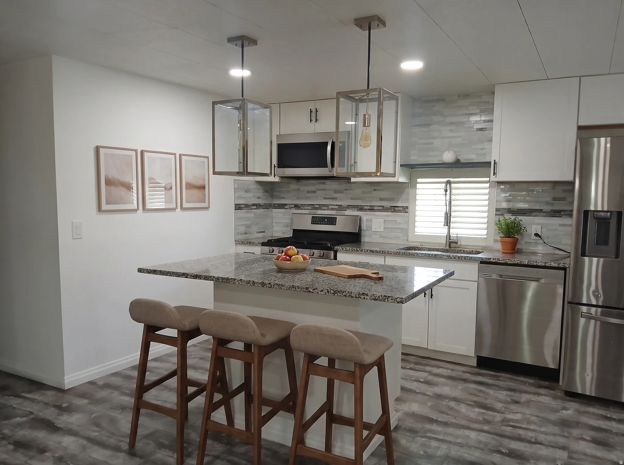 Kitchen featuring a central island with countertop seating, white cabinetry, stainless steel appliances, and wood-finish flooring