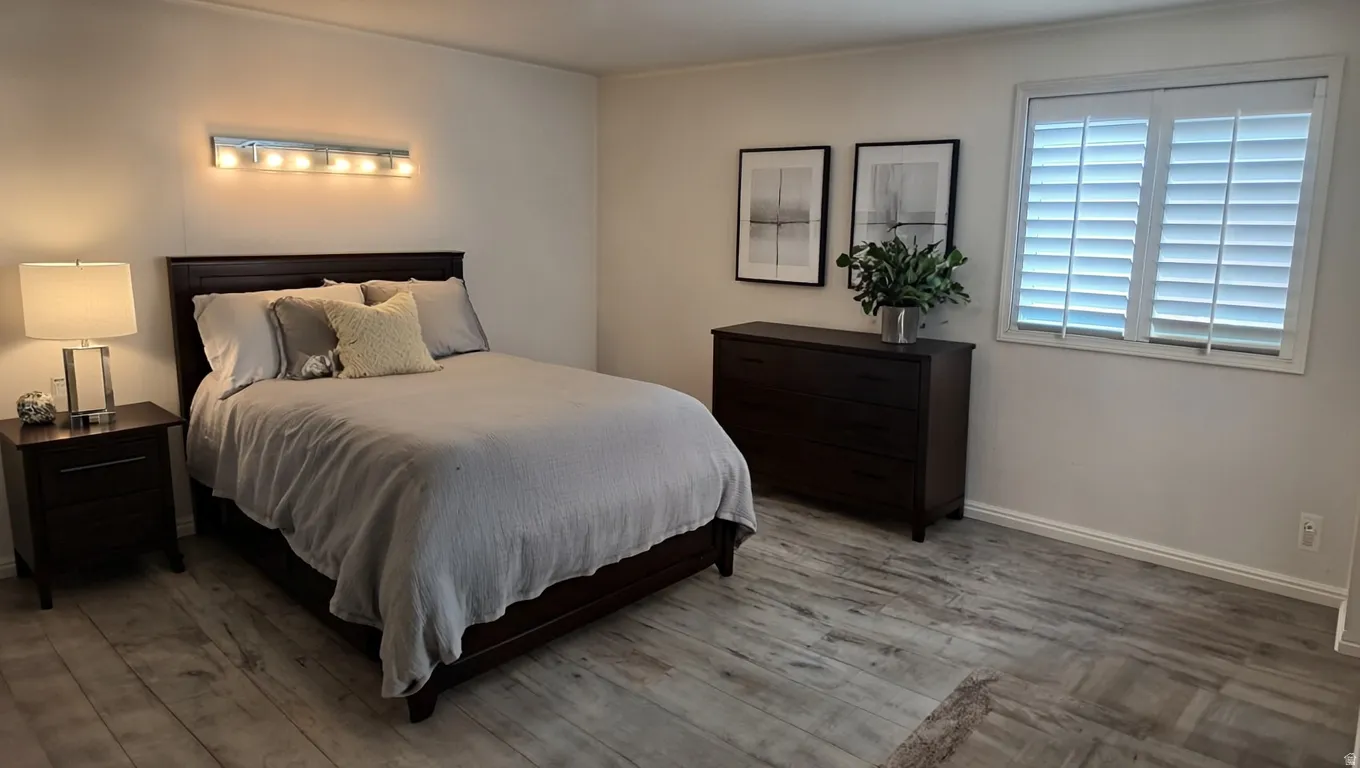 White walls featuring wood-finish flooring, a window with plantation shutters, and a wall-mounted light fixture