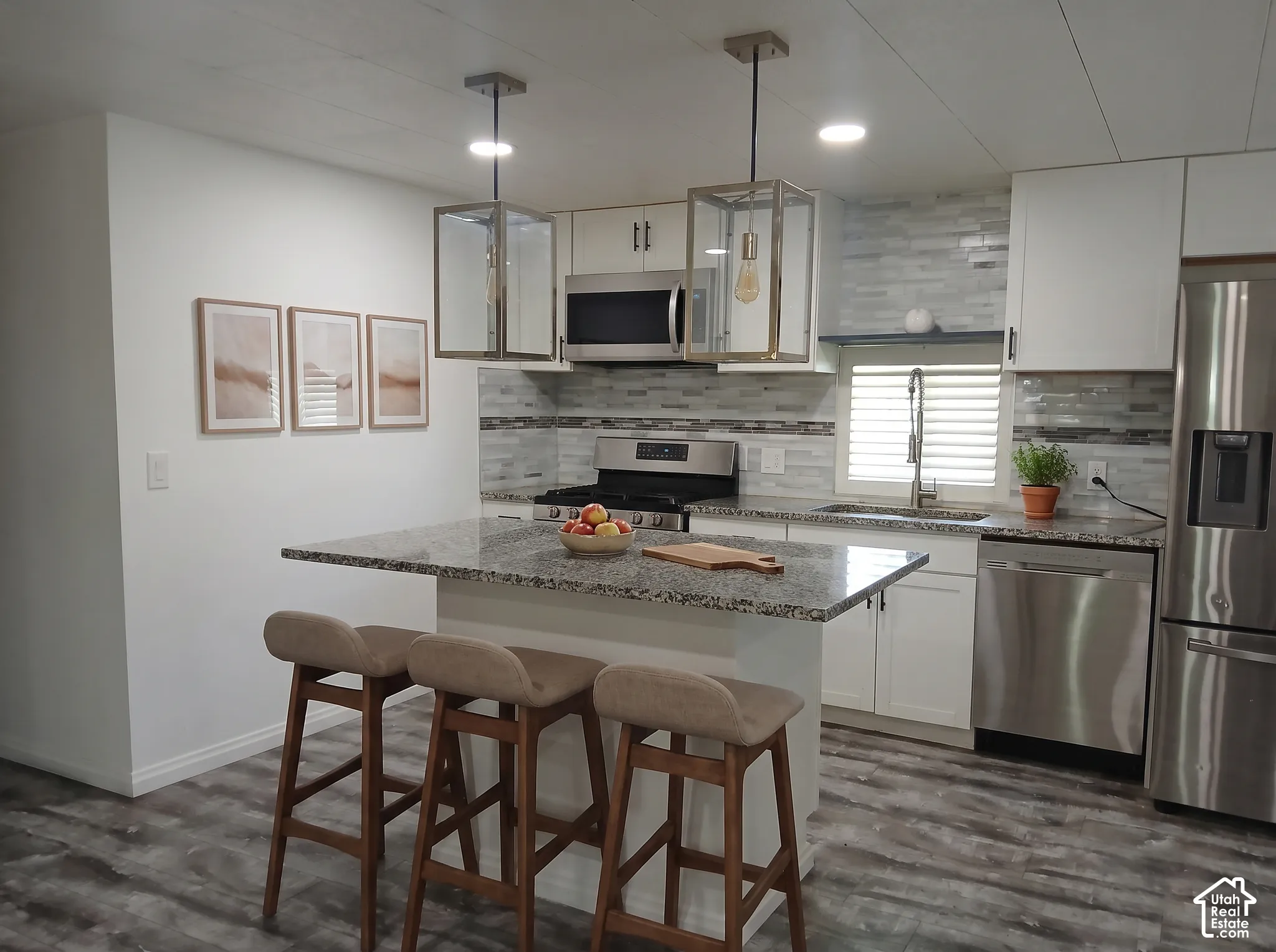 Kitchen featuring a central island with countertop seating, white cabinetry, stainless steel appliances, and wood-finish flooring