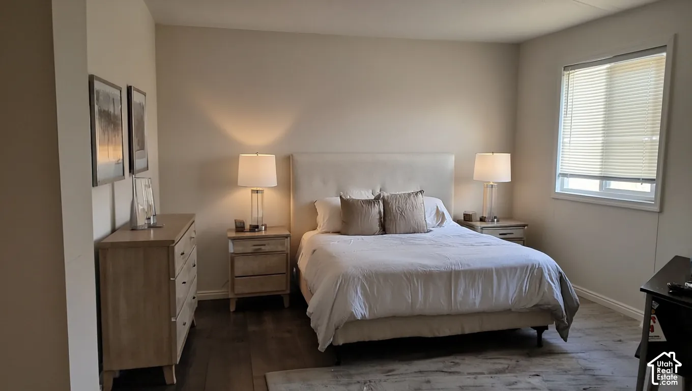 Spacious room featuring wood-finish flooring, light-colored walls, and a large window with blinds
