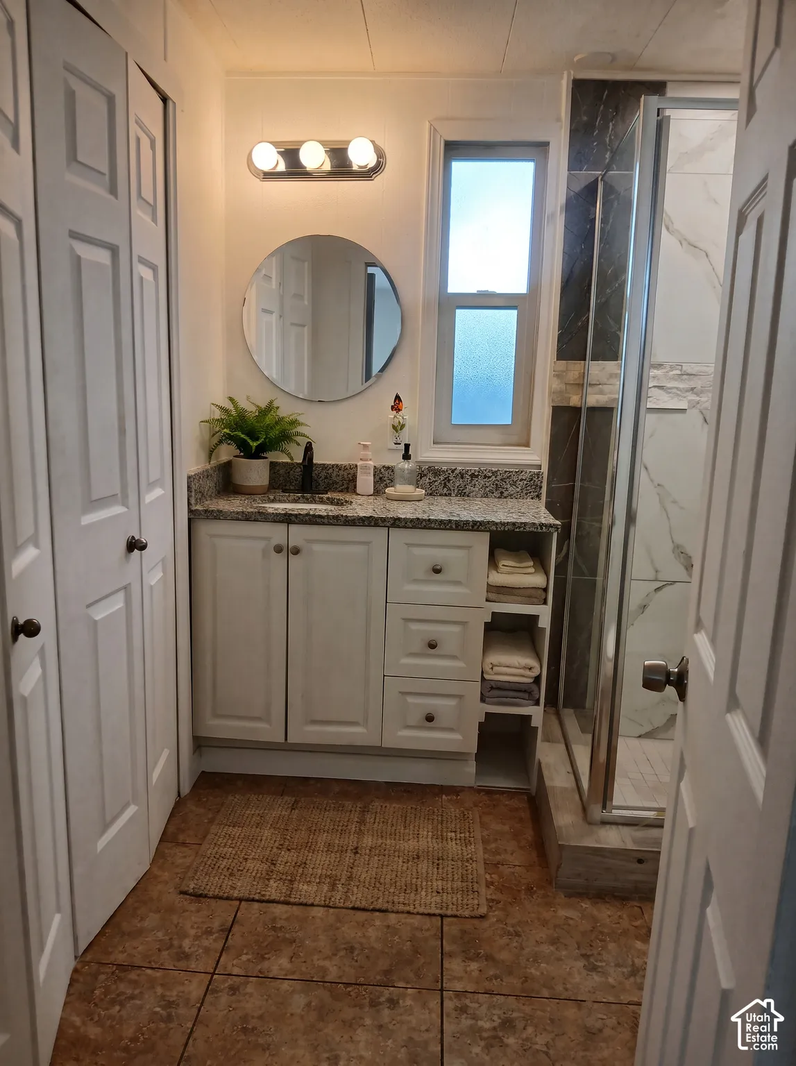 Bathroom featuring a white vanity with a granite-style countertop, a round mirror, and a three-light fixture
