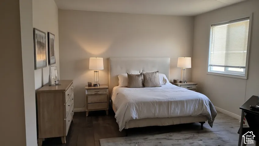 Spacious room featuring wood-finish flooring, light-colored walls, and a large window with blinds