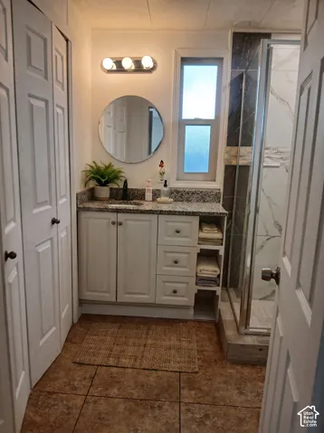 Bathroom featuring a white vanity with a granite-style countertop, a round mirror, and a three-light fixture