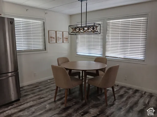 Spacious dining area featuring wood-finish flooring, multiple windows with blinds, and a contemporary linear chandelier