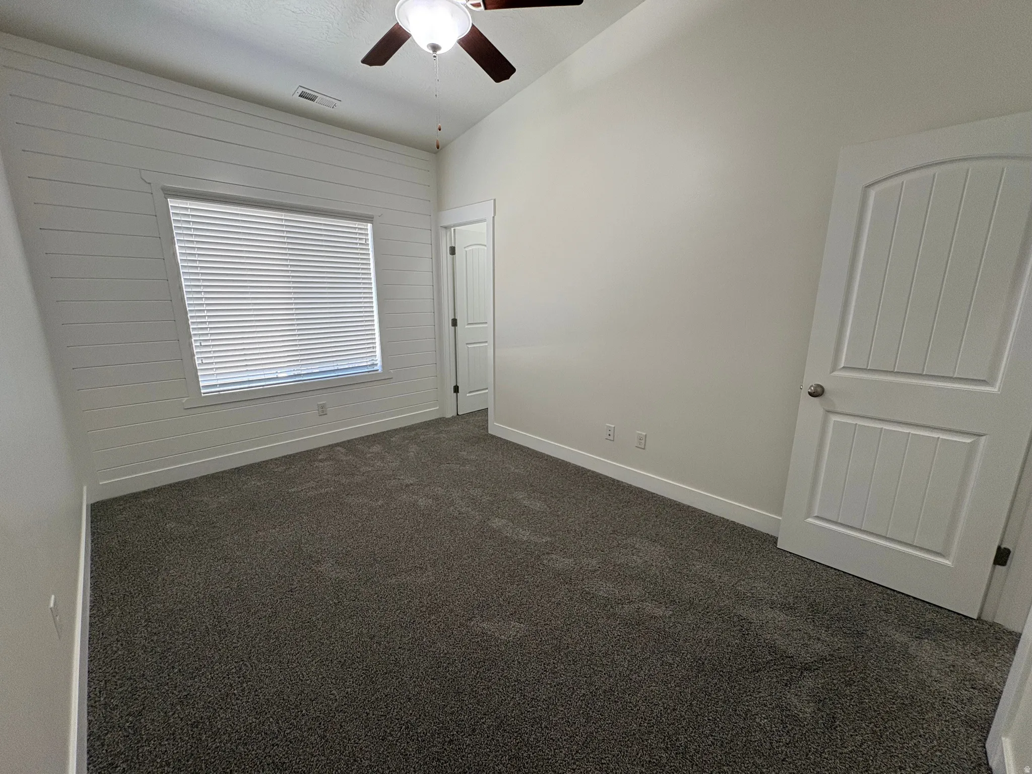 Vaulted ceiling with a ceiling fan, horizontal shiplap accent wall, neutral carpeting, and a panel door