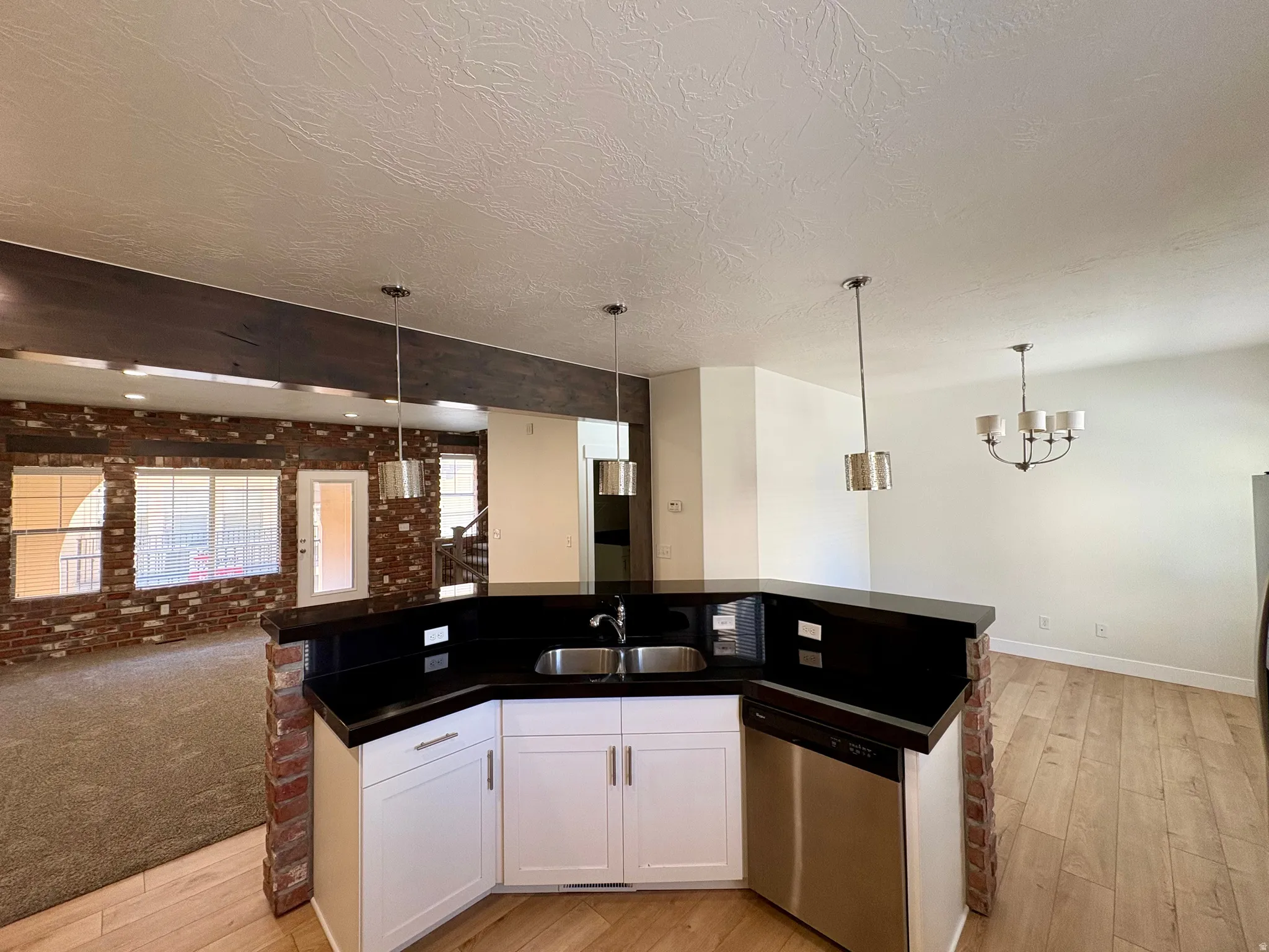 Kitchen island with dark countertops, stainless steel sink, and integrated dishwasher