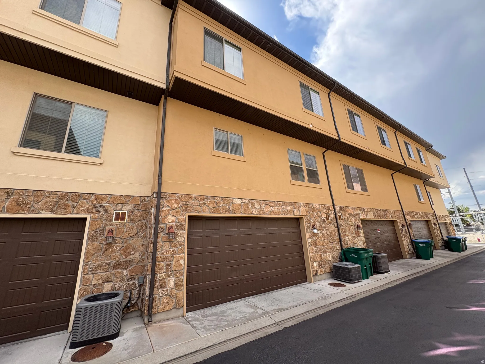 Multi-story exterior with stucco and stone veneer, multiple garages featuring brown doors, and exterior wall sconces