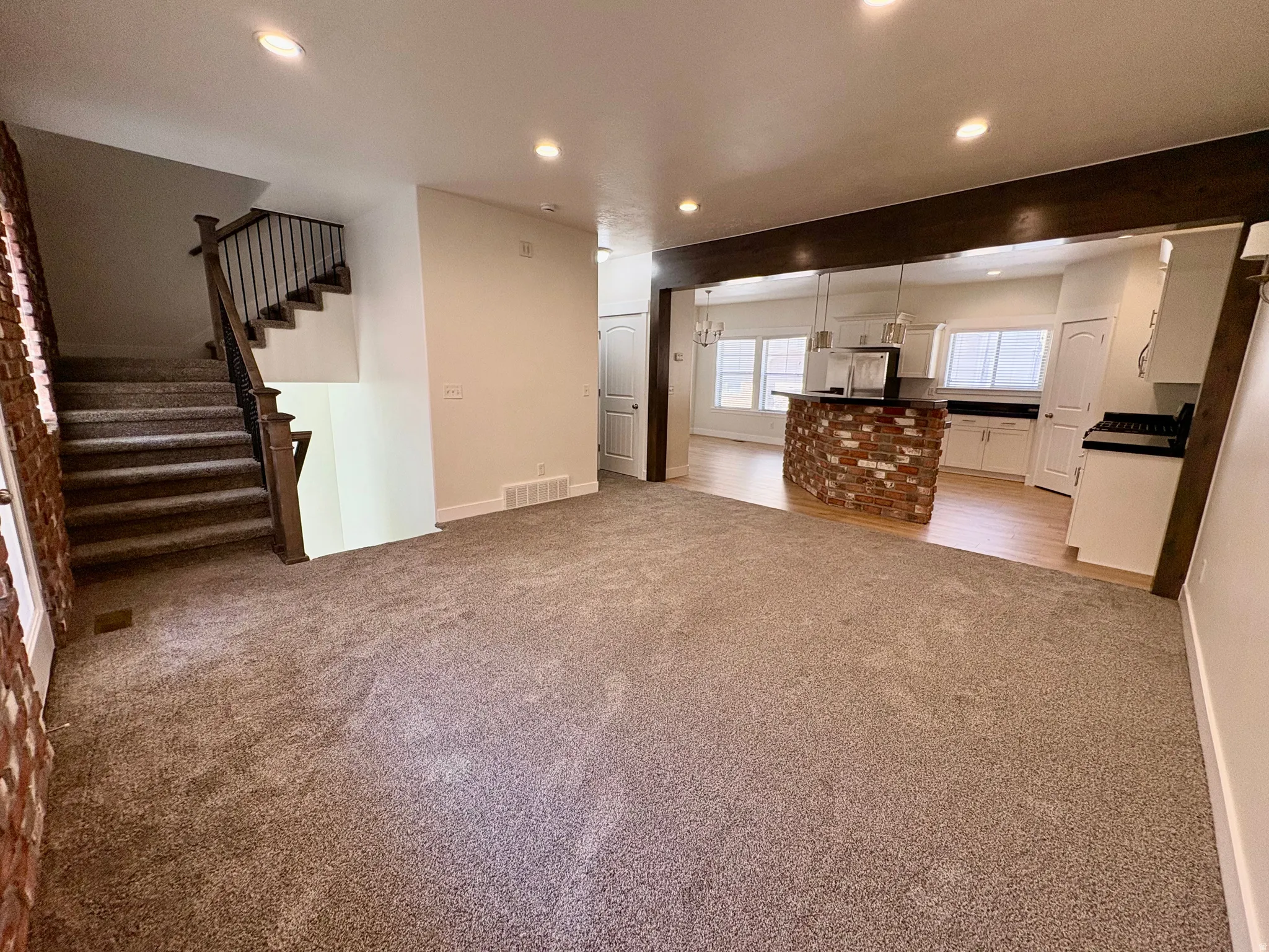 Expansive carpeted living space with recessed lighting and a brick accent wall