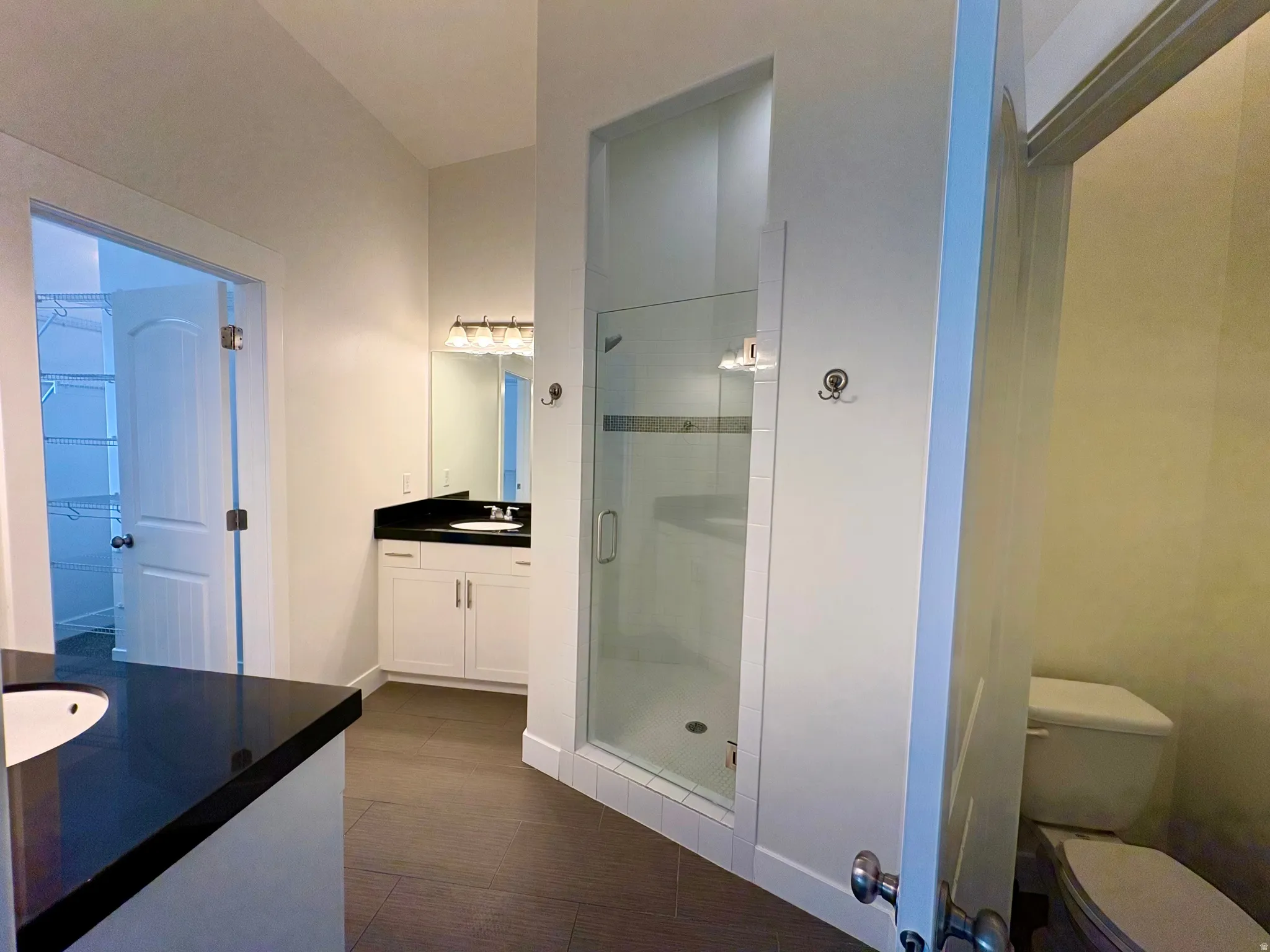 Dual white vanities with dark countertops, a glass-enclosed shower, a separate water closet, and wood-finish flooring