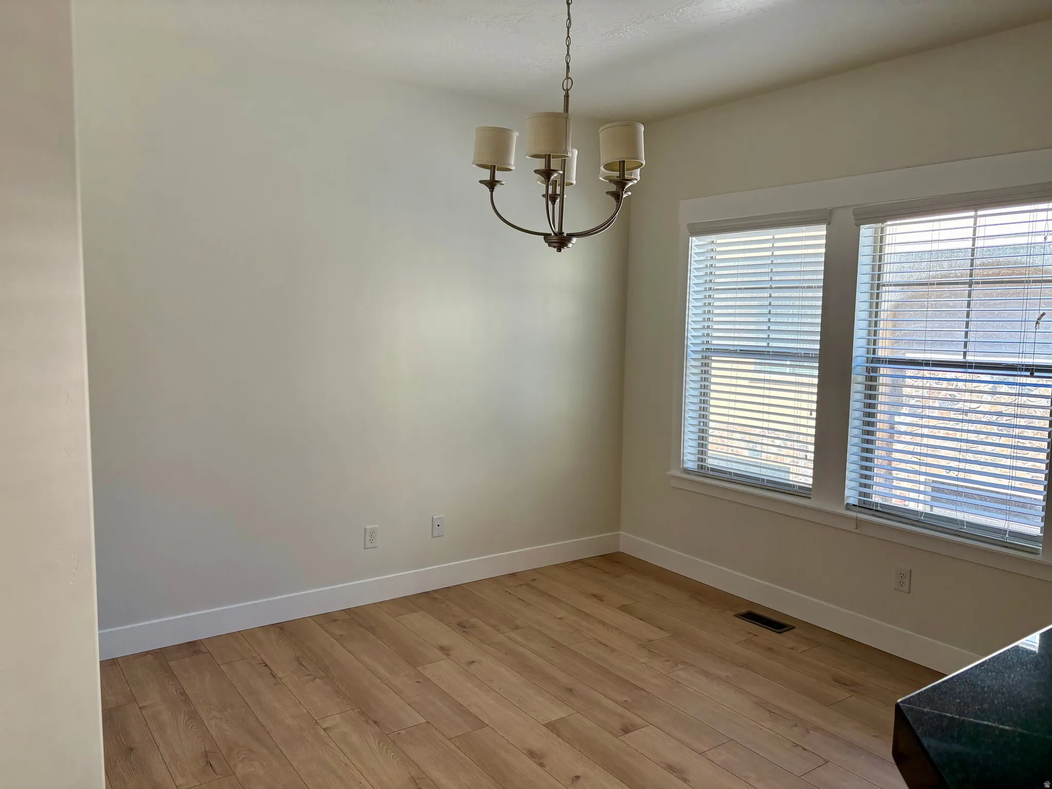 Recessed lighting with a bronze finish chandelier, wood-finish flooring, and multiple windows with blinds