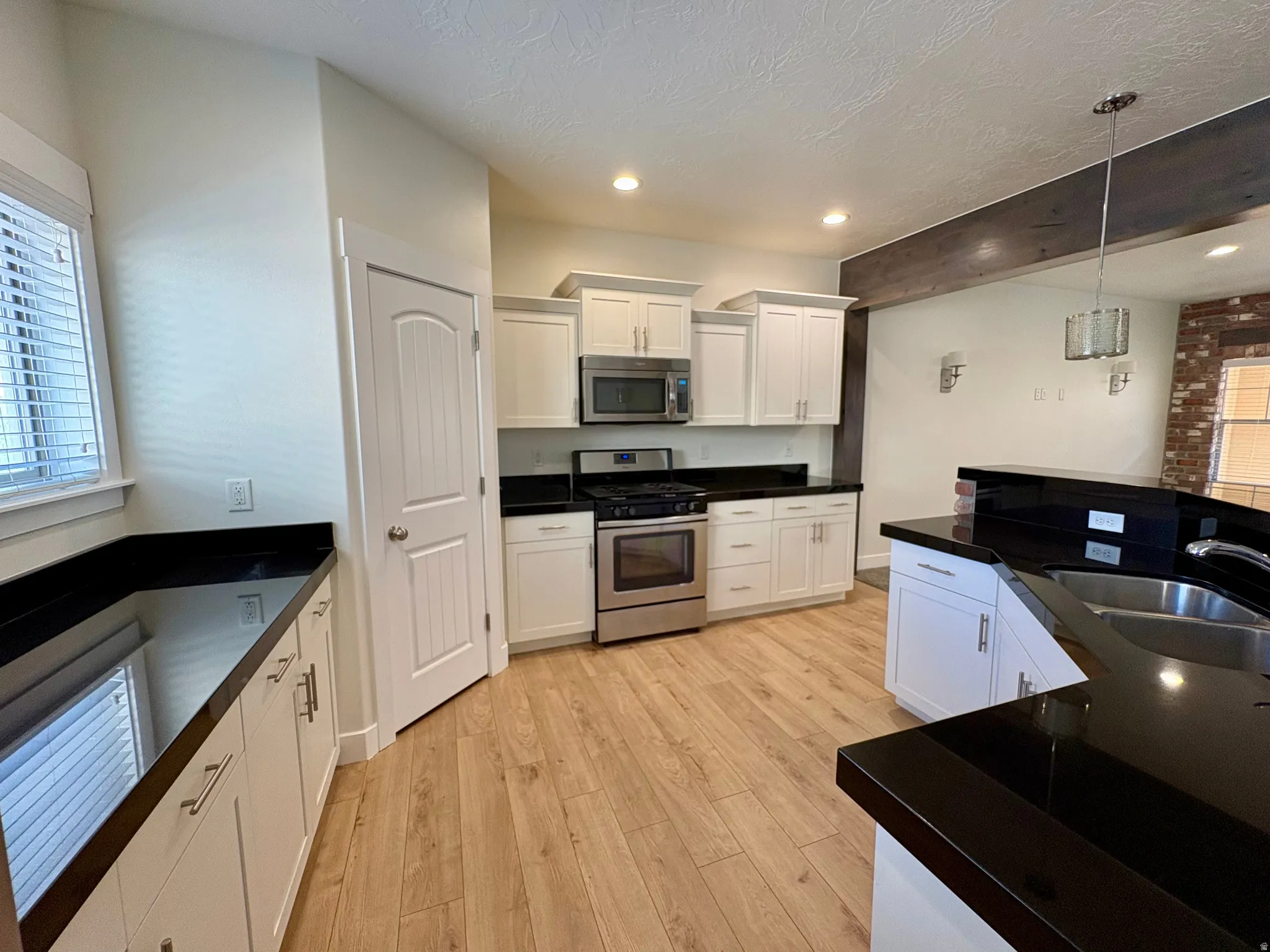 Kitchen featuring white cabinetry, dark countertops, stainless steel appliances, wood-finish flooring, and recessed lighting