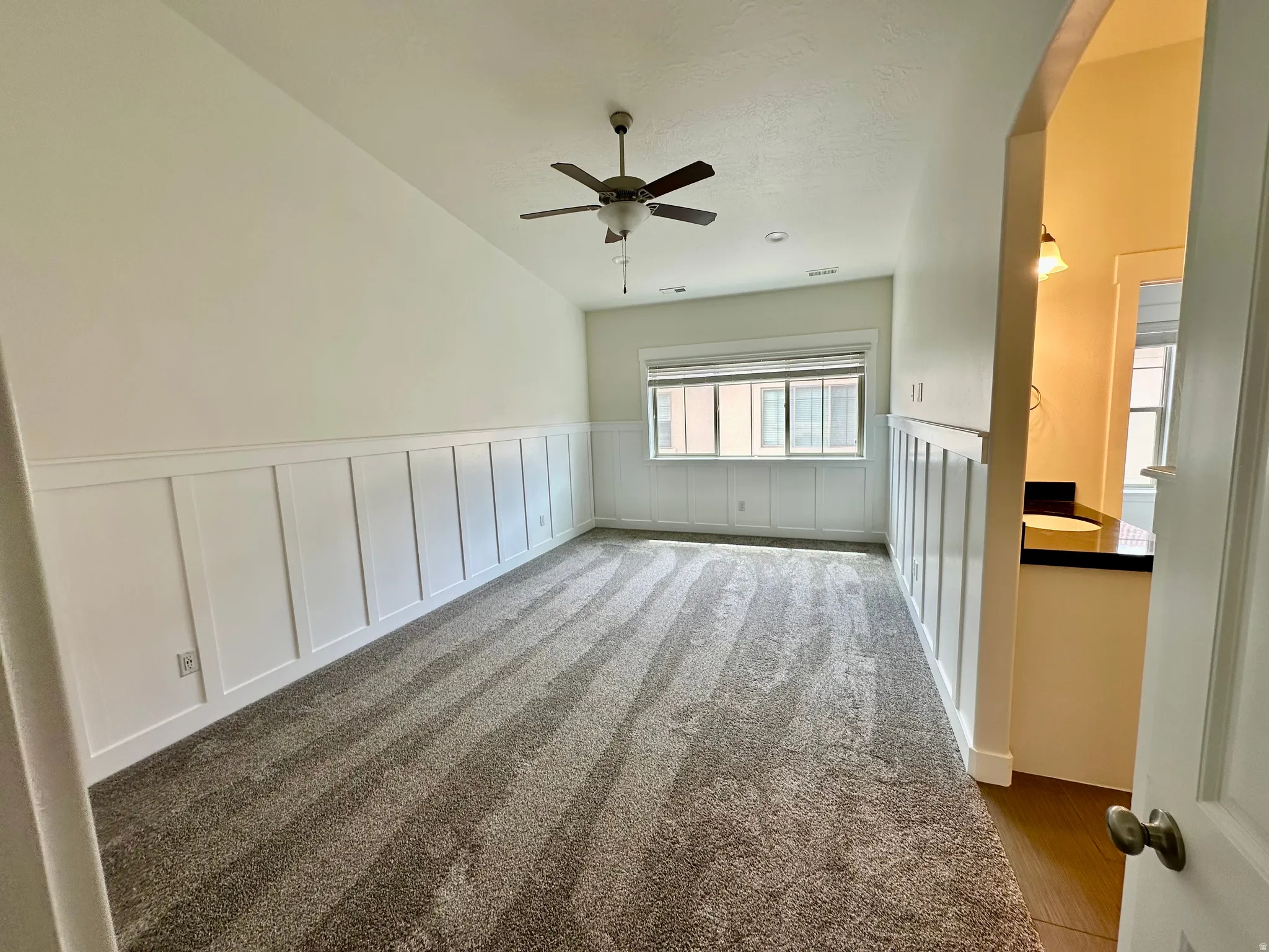 Vaulted ceiling with a ceiling fan, board and batten wall detailing, carpeted flooring, and window treatments