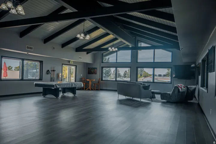 Vaulted ceiling with exposed beams, wood-finish flooring, multiple large windows, and a double glass door