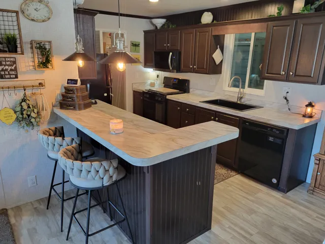 Contemporary kitchen featuring dark cabinetry with brushed metal hardware, light wood-finish countertops extending across an oversized island, and stainless steel appliances including a built-in range and refrigerator