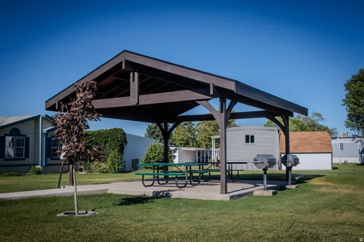 Covered outdoor pavilion featuring a concrete pad, built-in picnic tables, and two permanent barbecue grills, all set on a manicured lawn