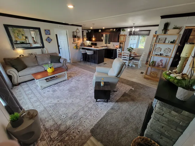 Open-concept living space featuring wood-look flooring, a stone-faced fireplace surround, and recessed lighting