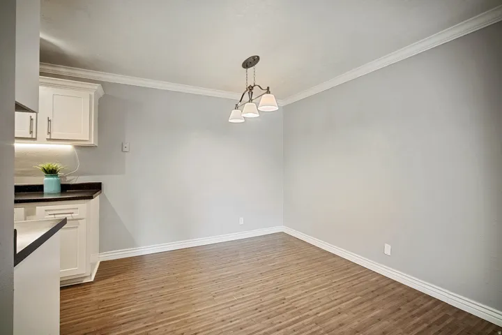 Wood-finish flooring, white crown molding, white baseboards, and a three-light chandelier