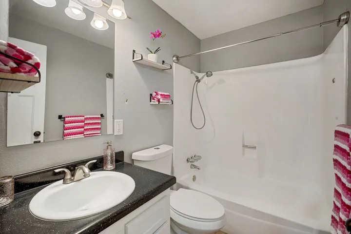 Bathroom featuring a single vanity with a black countertop, oval undermount sink, and a combination shower/tub with a handheld showerhead