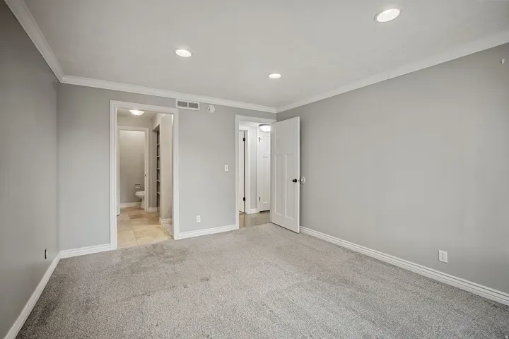 Recessed lighting, crown molding, gray painted walls, carpeted flooring, and a paneled door with dark hardware