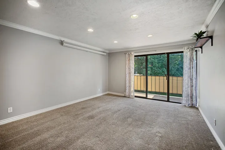 Recessed lighting, crown molding, gray carpeting, sliding glass doors, and a built-in wall shelf