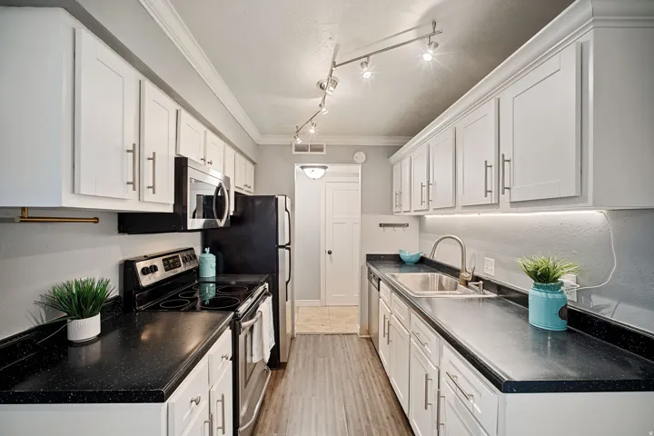 Galley kitchen featuring white cabinetry, dark countertops, stainless steel appliances, and wood-finish flooring