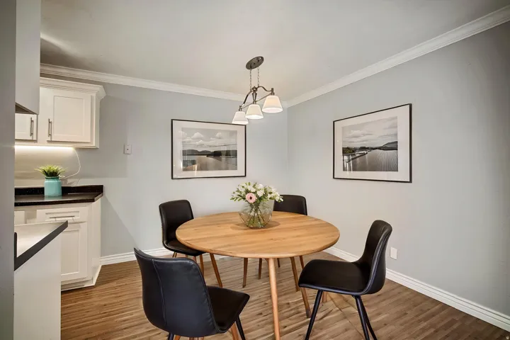 Crown molding, wood-finish flooring, white cabinetry, dark countertops, and a multi-light chandelier