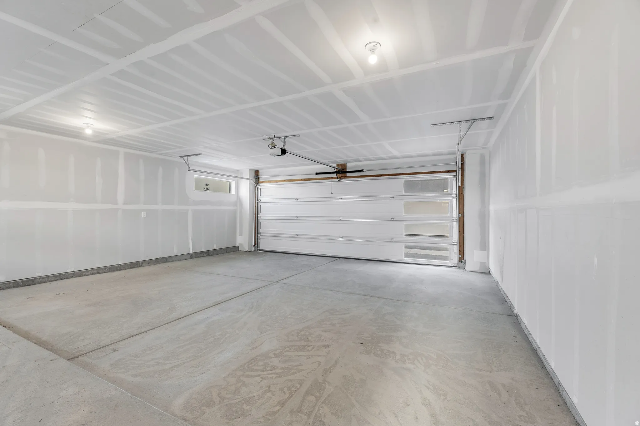 Spacious attached garage featuring concrete flooring, white drywall construction, overhead garage door with hardware, ceiling-mounted opener system, and recessed lighting throughout