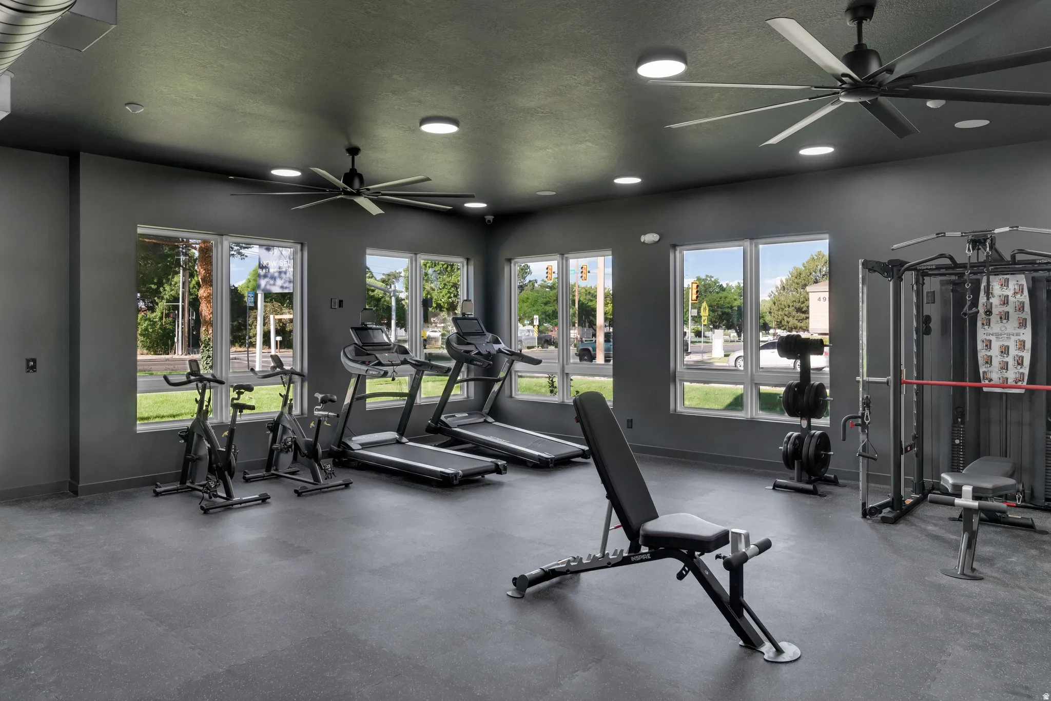 Expansive fitness area with resilient flooring, multiple large windows, recessed lighting, and dual ceiling fans