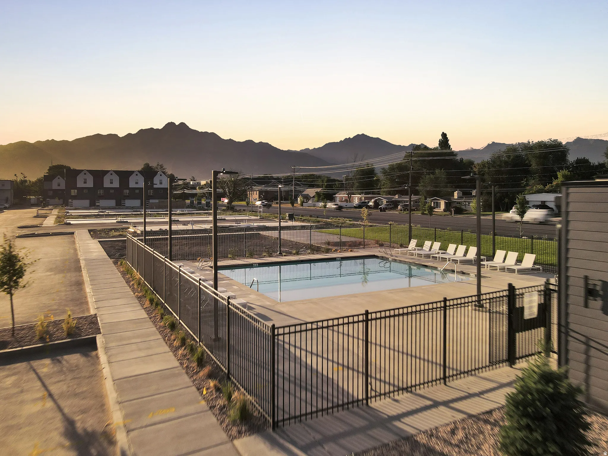 Resort-style community pool with black metal perimeter fencing, concrete decking, and lounge seating