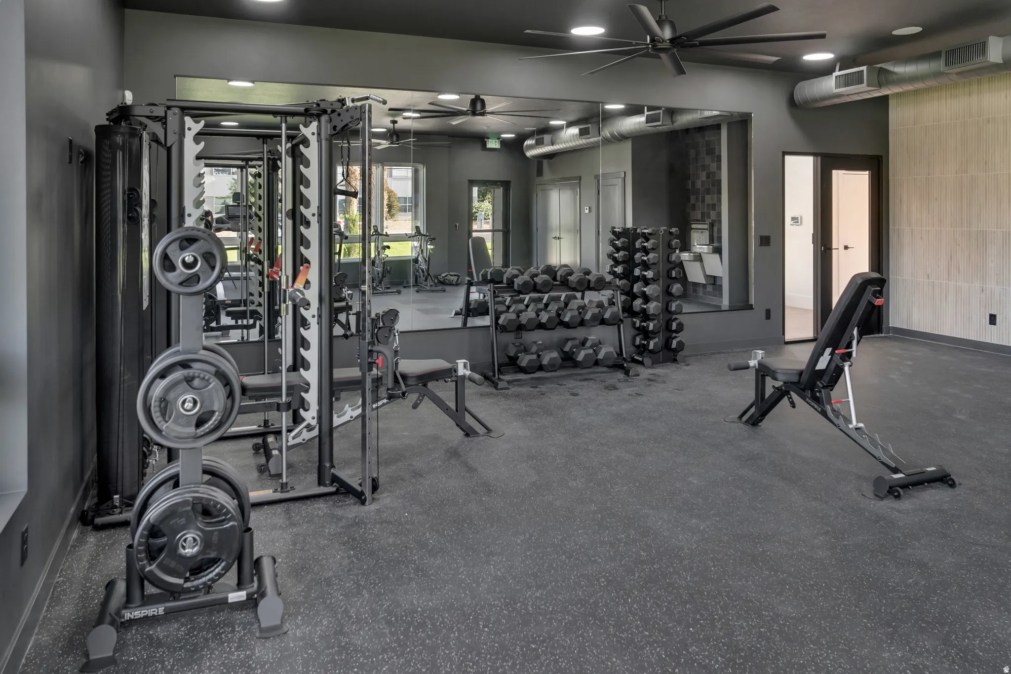 State-of-the-art fitness facility featuring a comprehensive cable machine system, stacked dumbbell rack with multiple weight options, stationary cycling equipment, and mirrored walls throughout
