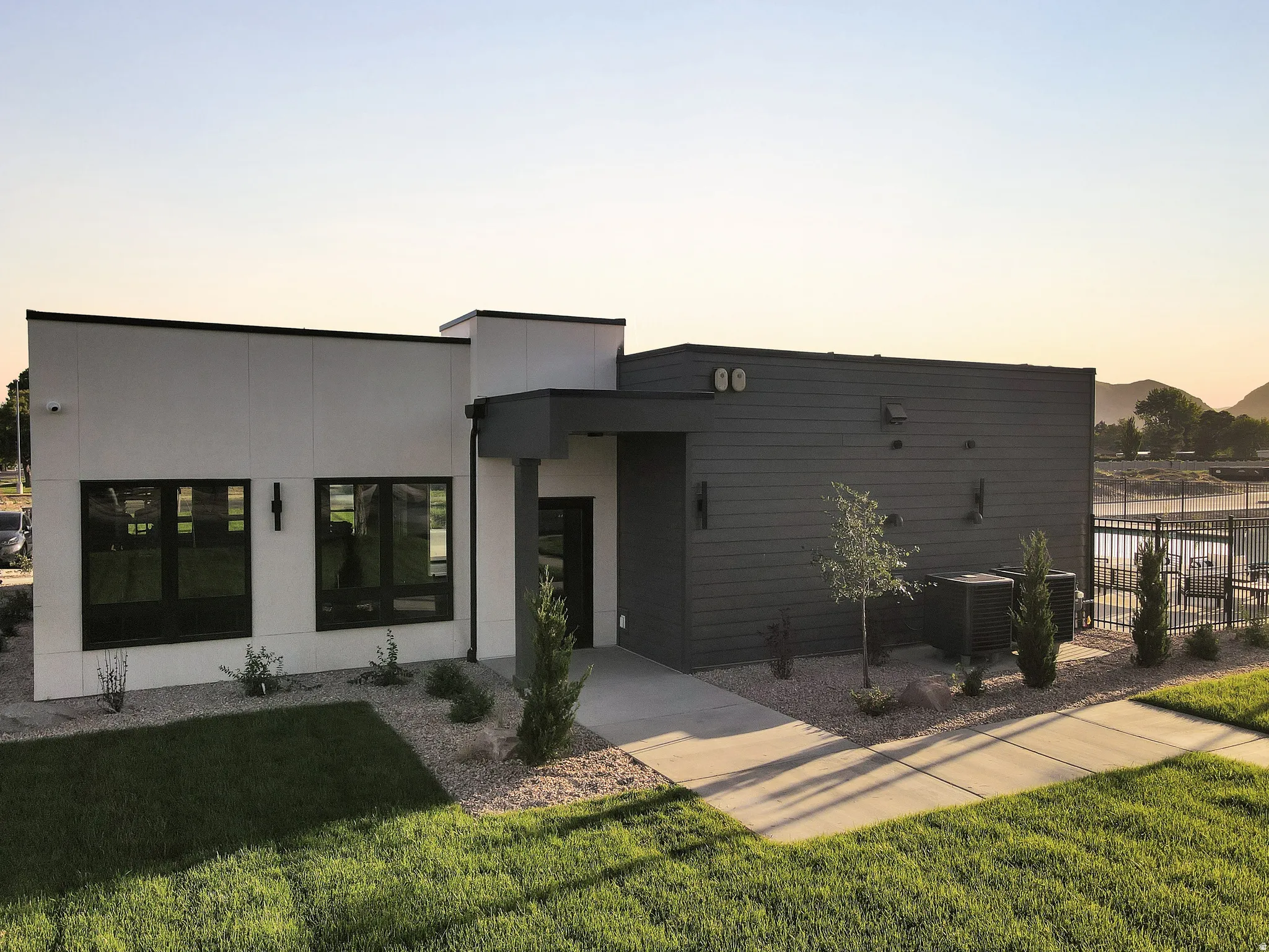 Modern architectural design featuring a clean-lined facade with mixed material finishes—white and charcoal exterior cladding—complemented by expansive black-framed windows and glass doors