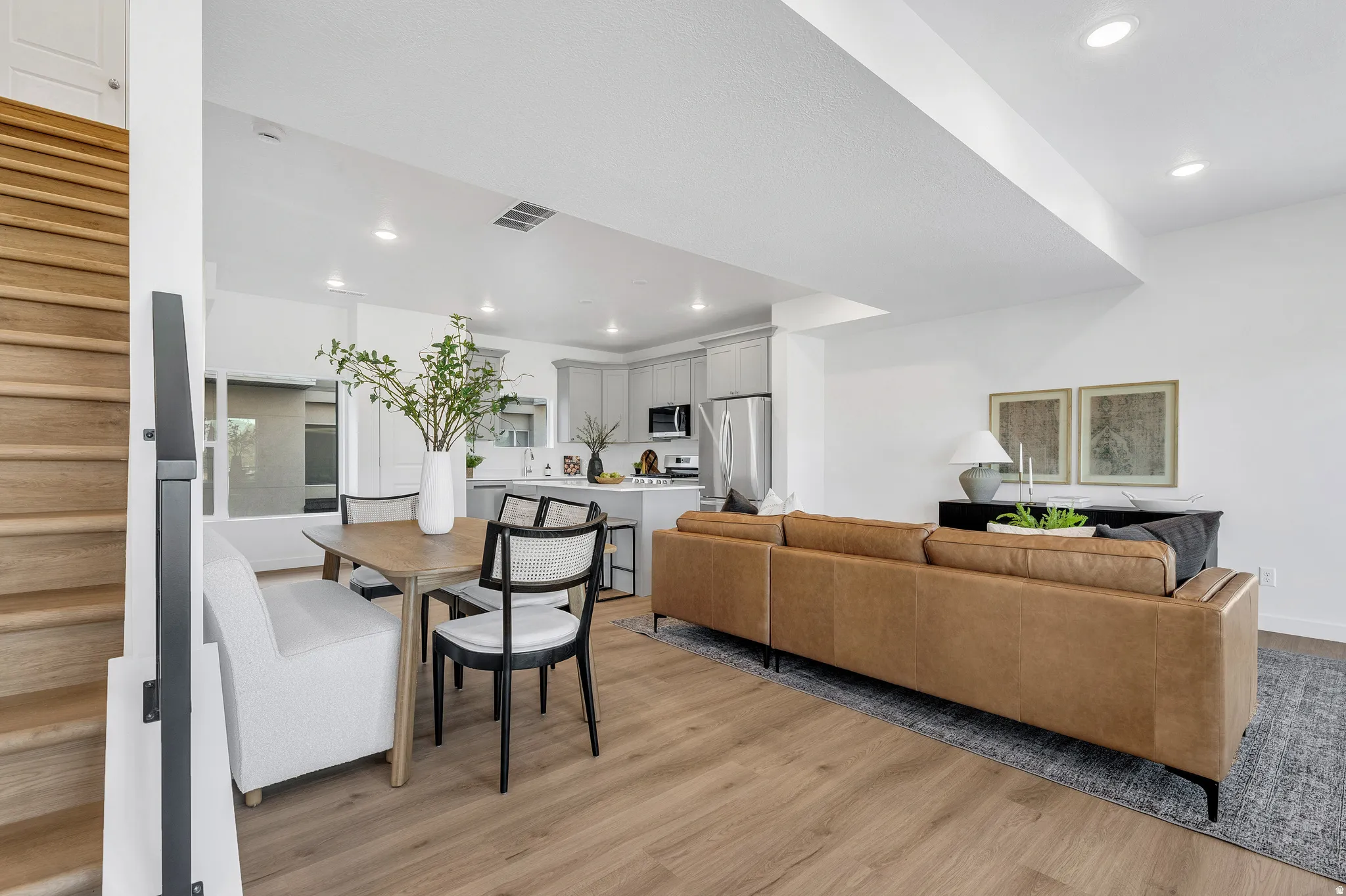 Wood-finish flooring throughout, recessed lighting, sleek black metal stair railing, and a kitchen featuring light gray cabinetry and stainless steel appliances