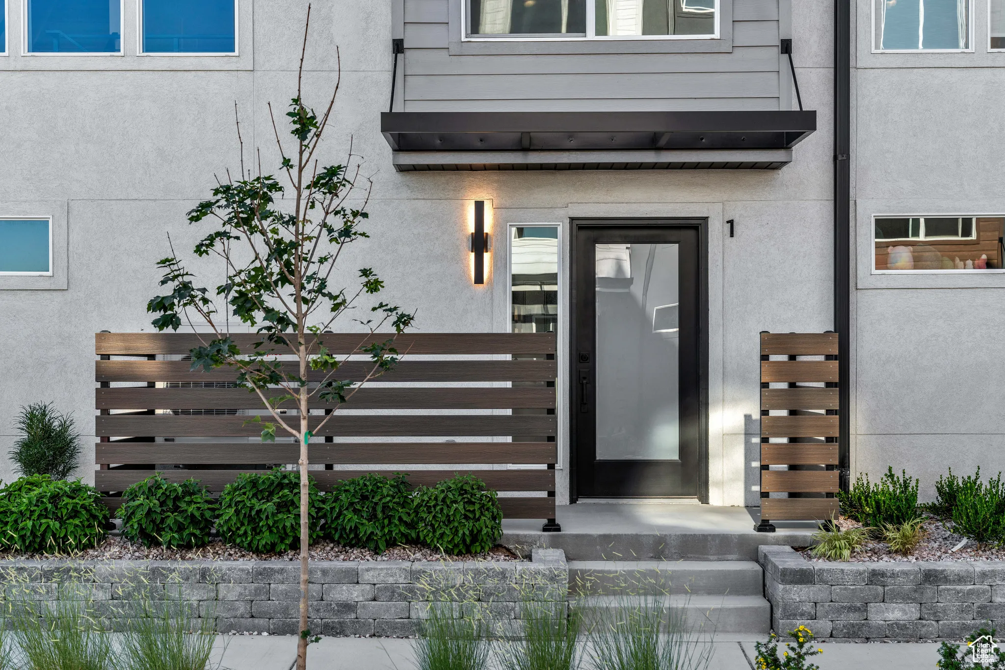 Modern front entrance featuring a horizontal wood-slat privacy fence with integrated planter beds, concrete stepping stone pathway, and contemporary black-framed glass door with sidelights