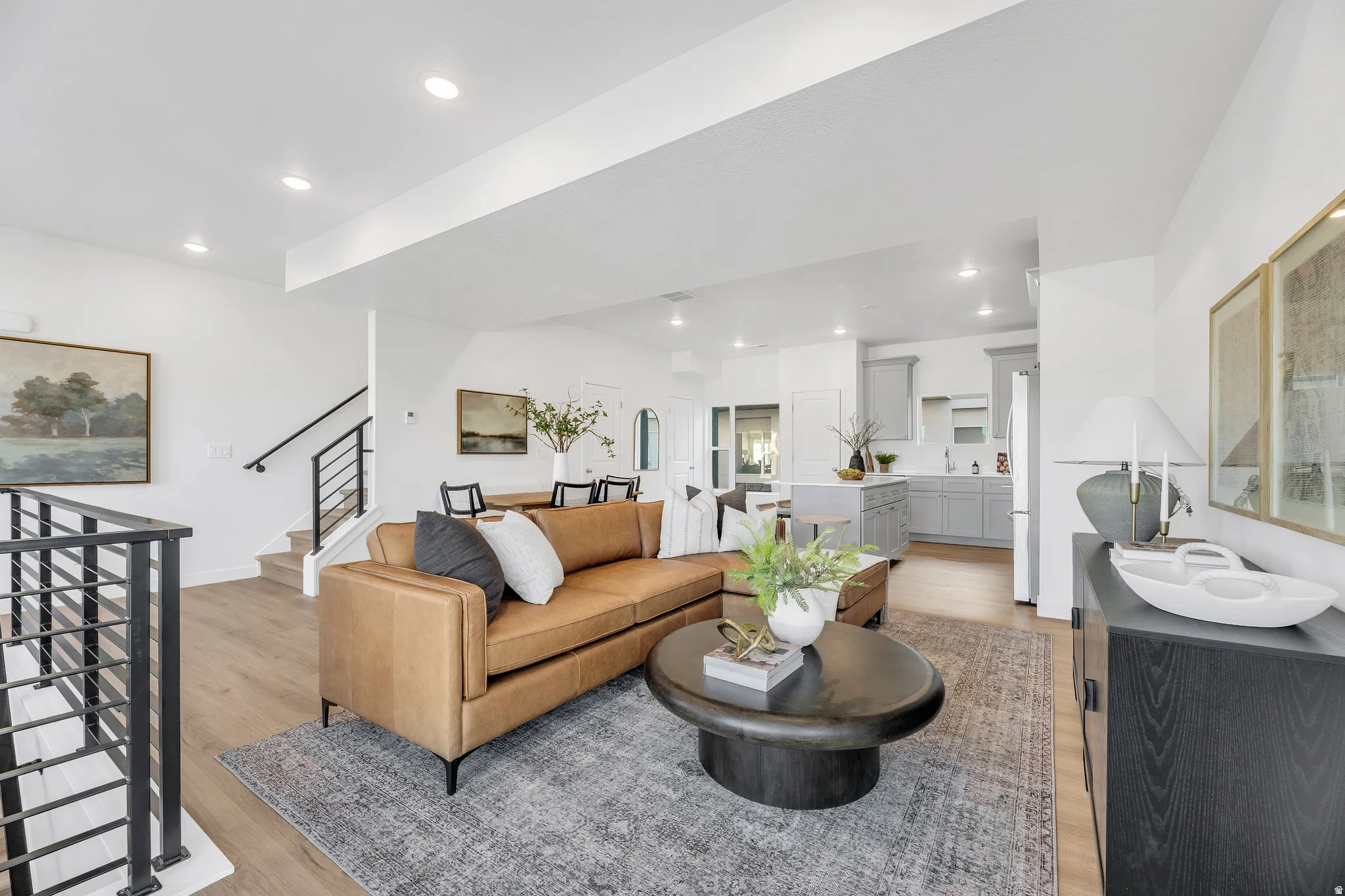Open-concept living area featuring a cognac leather sofa, dark wood-finish oval coffee table, and neutral area rug anchoring the space