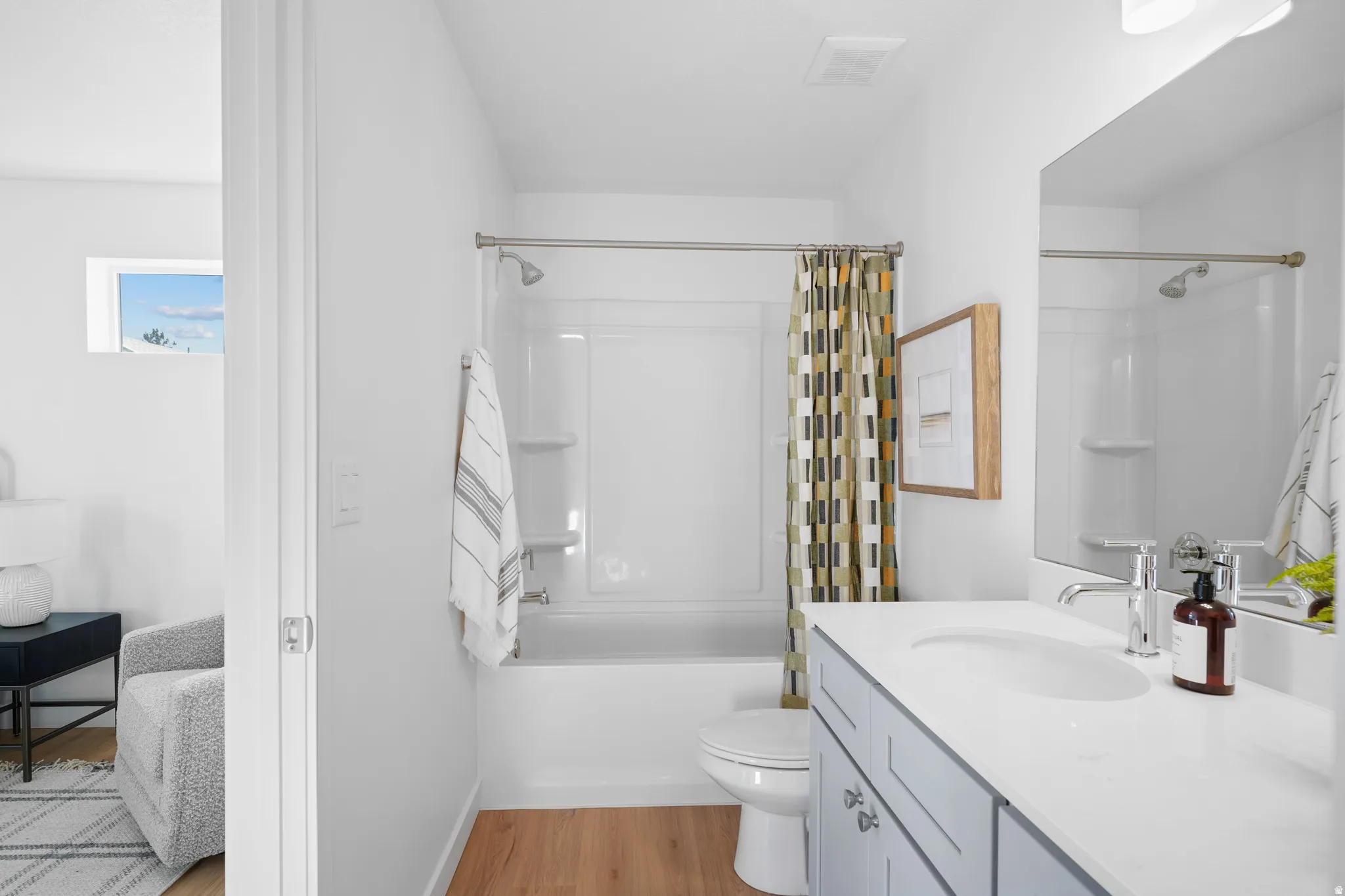 Bright and spa-like primary bathroom featuring a double-sink vanity with white cabinetry and quartz countertop, frameless glass shower enclosure with subway tile surround, wood-finish flooring, and brushed nickel fixtures throughout