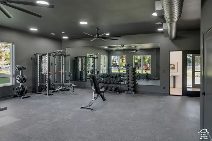 State-of-the-art fitness facility featuring multiple strength training stations with glass enclosures, polished concrete flooring, recessed and pendant ceiling lighting, ceiling fan, and expansive windows overlooking landscaped grounds