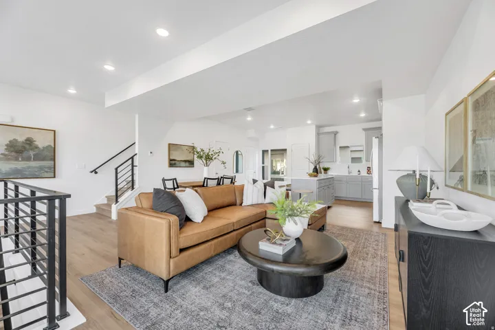 Open-concept living area featuring a cognac leather sofa, dark wood-finish oval coffee table, and neutral area rug anchoring the space