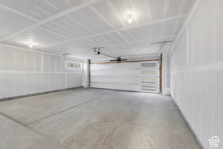 Spacious attached garage featuring concrete flooring, white drywall construction, overhead garage door with hardware, ceiling-mounted opener system, and recessed lighting throughout