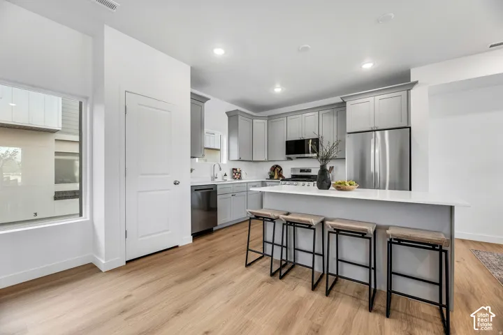 Modern kitchen featuring light wood-finish flooring, stainless steel appliances, grey cabinetry, a white countertop island, and recessed lighting